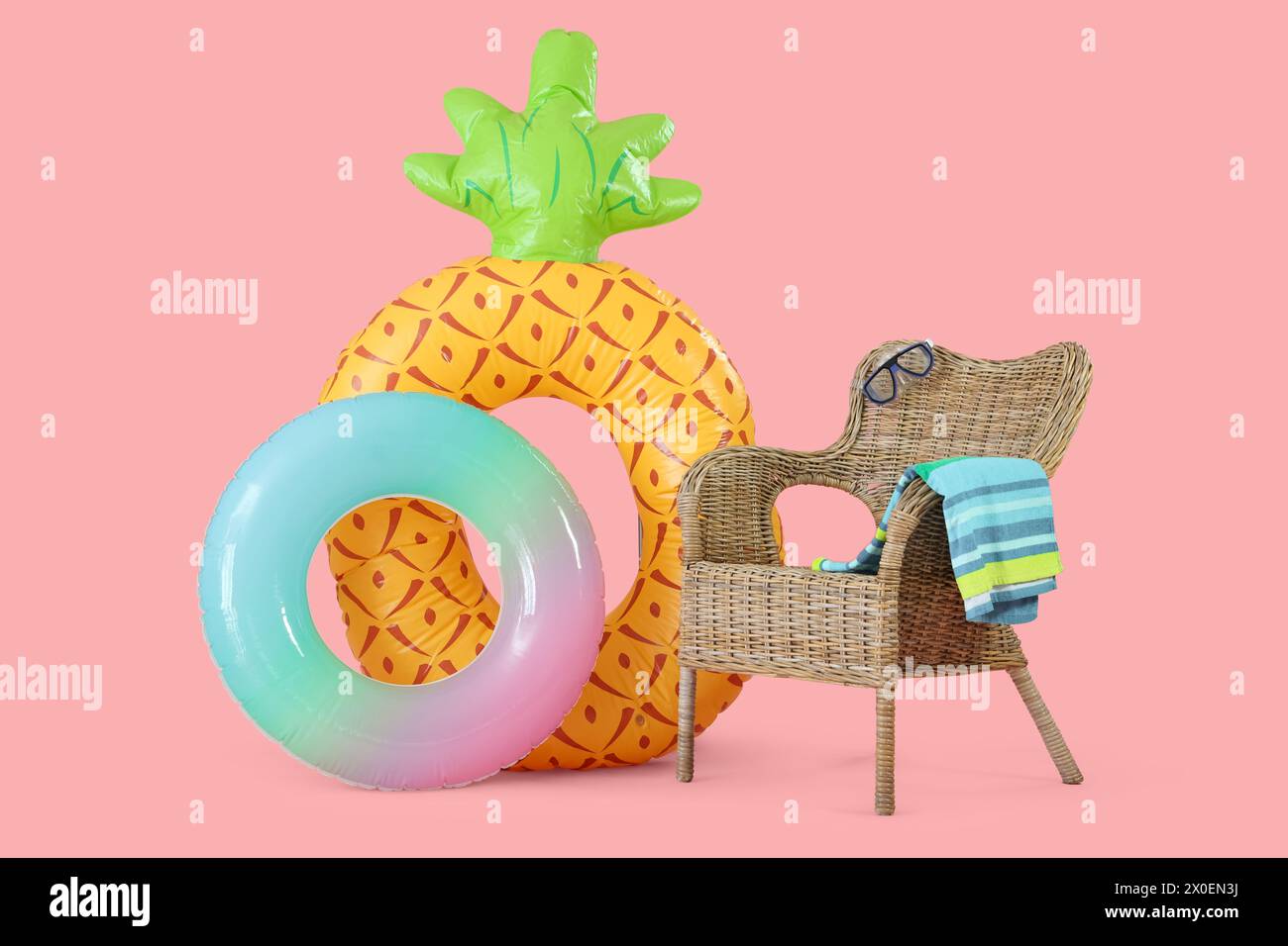 Inflatable rings and straw chair with snorkeling mask and towel on pink background Stock Photo