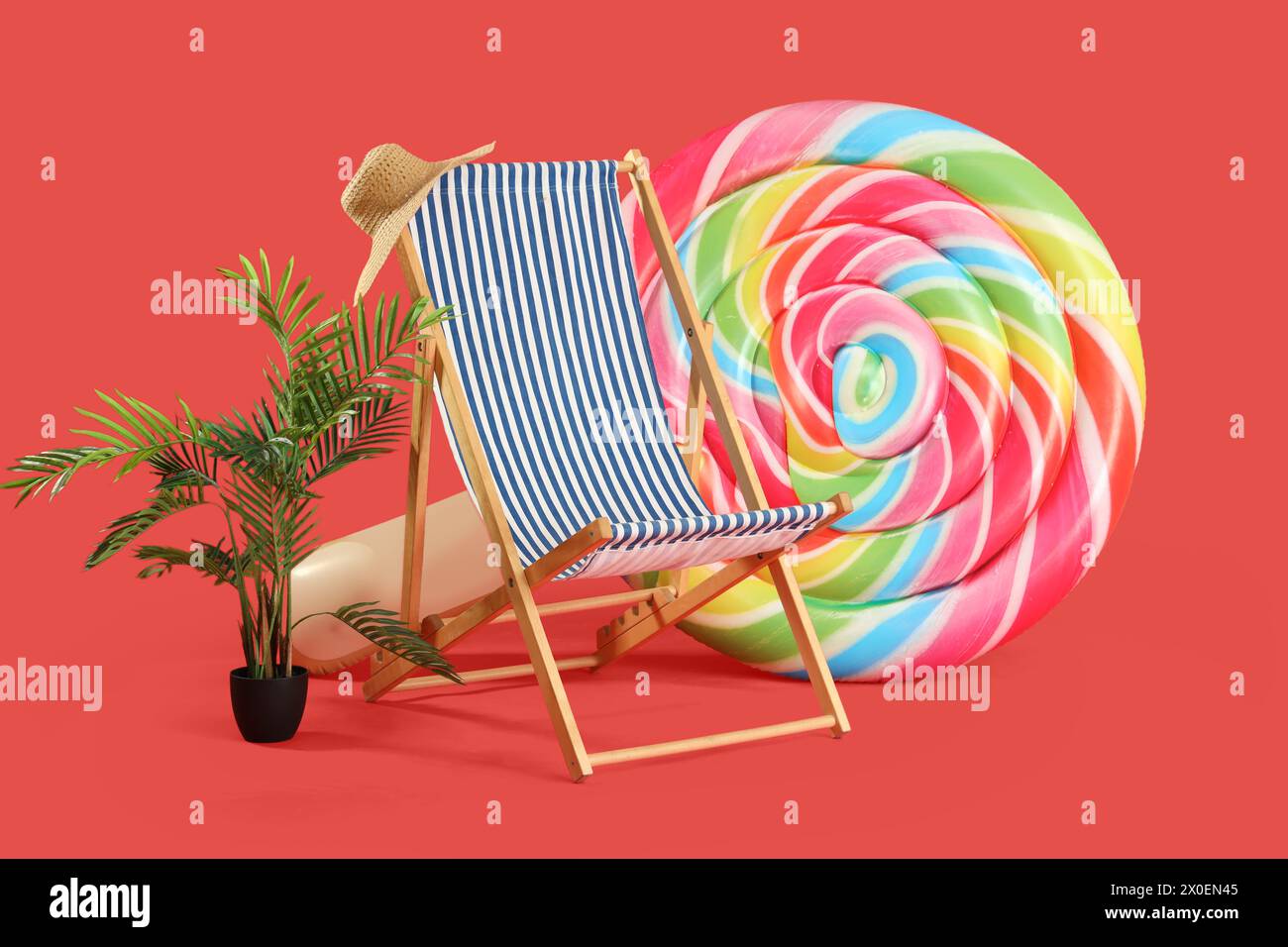 Sun lounger, plant and inflatable mattress in shape of candy on red background Stock Photo