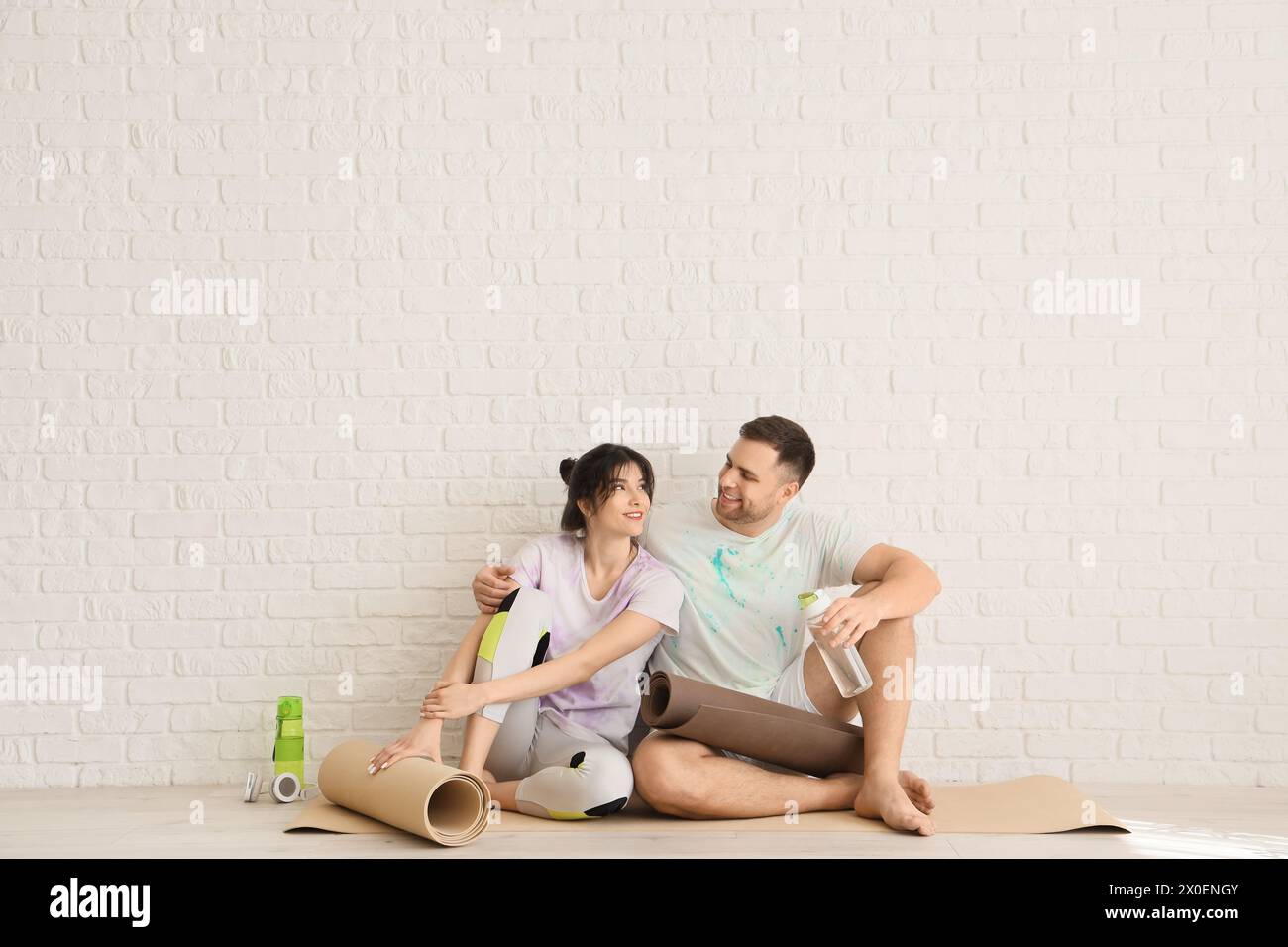 Sporty young couple sitting on yoga mat after training in light room Stock Photo