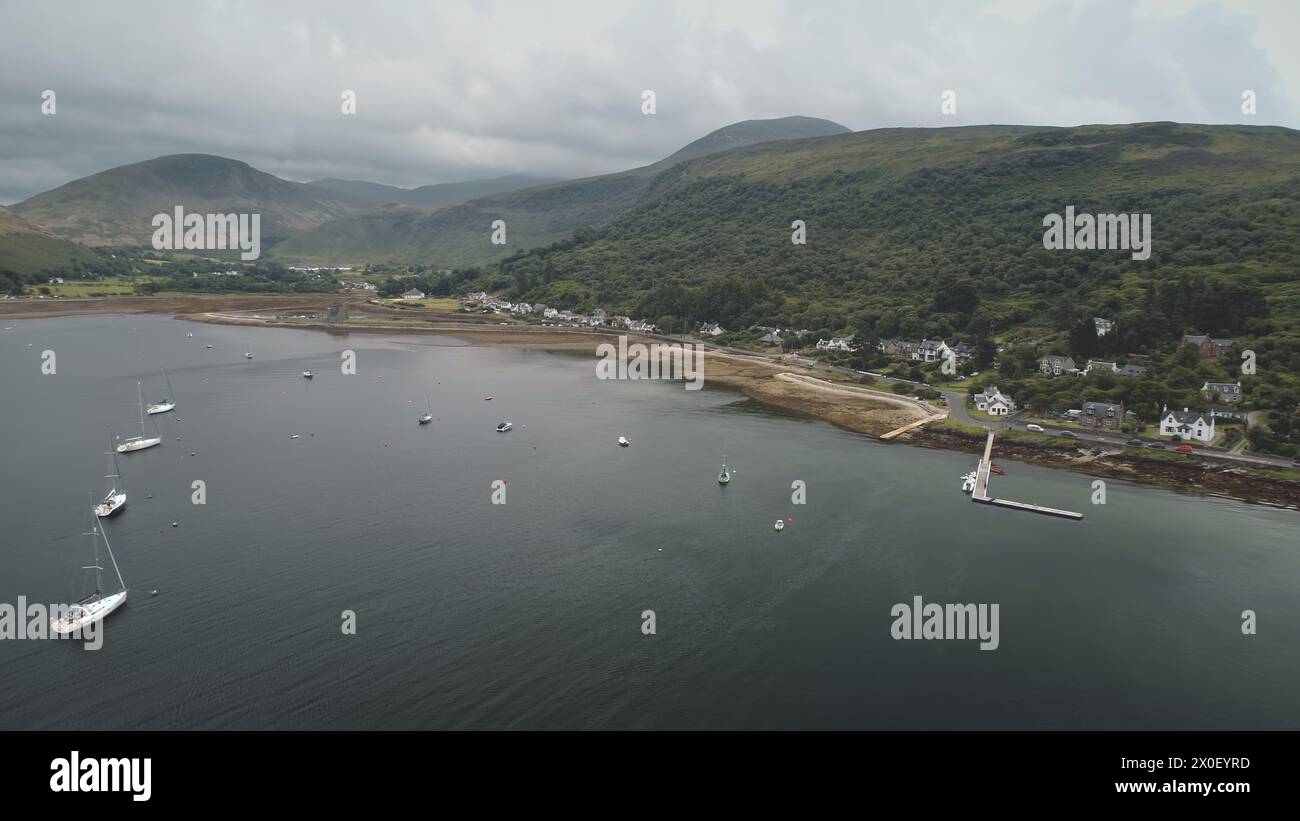 Yachts, ships at green mountain on ocean bay coast aerial. Nobody nature with serene seascape. Water transport at harbor of Arran Island, Scotland. Marine vacation at summer. Cinematic travel, tourism Stock Photo