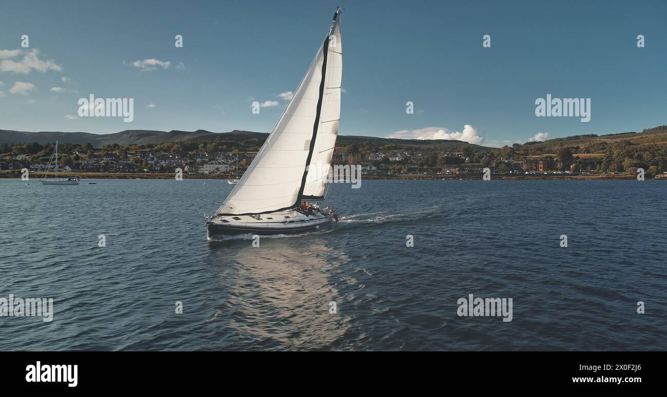 Regatta yacht sailing at pier town cityscape aerial. Sail boat cruise at open sea. Arran Island harbor with mountain shore. Passenger ship at ocean. Epic seascape at summer. Scotland, Europe Stock Photo