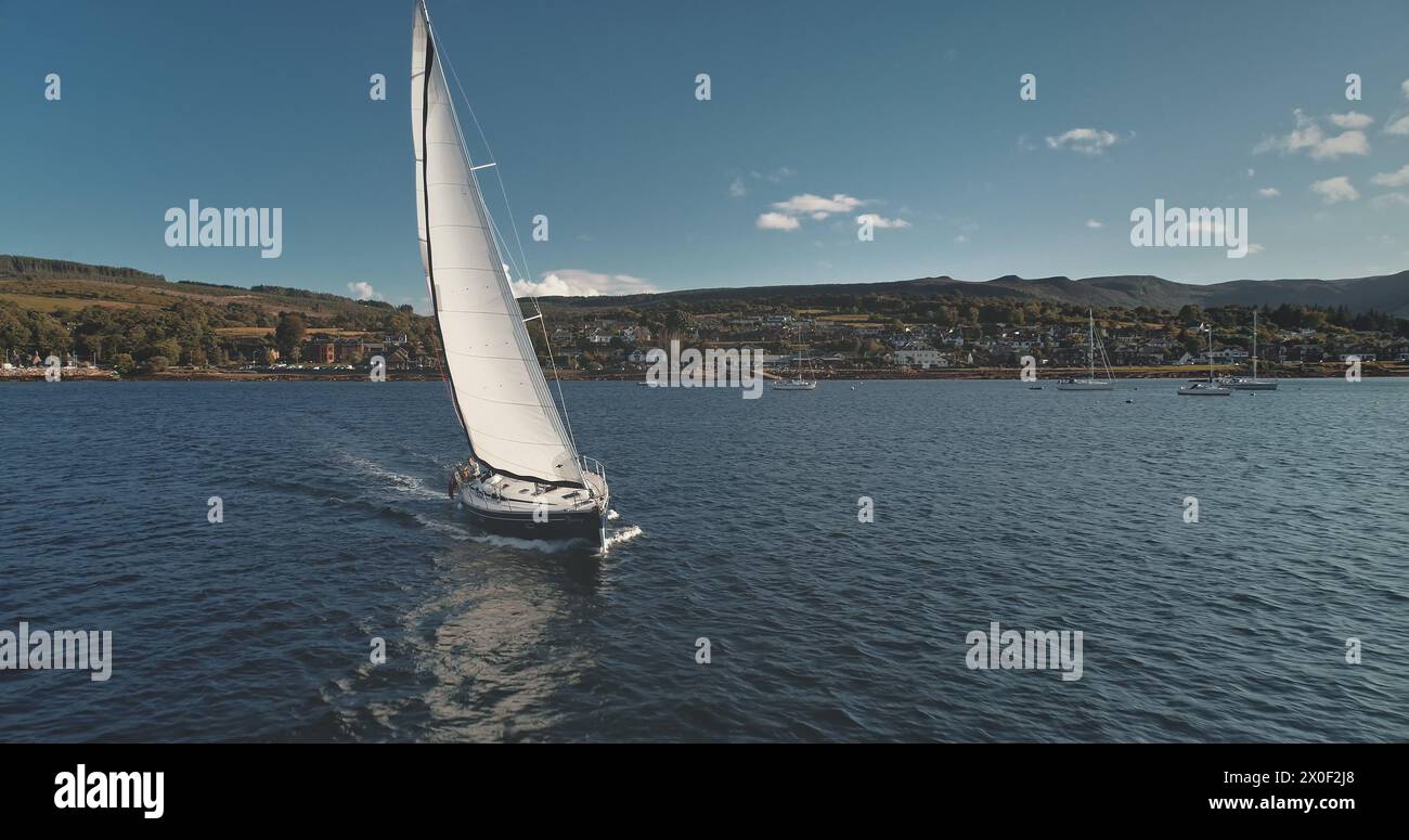 Luxury yacht at reflection at sea bay aerial. Nobody nature seascape. Amazing passenger sail boat at Brodick pier cityscape. Scotland landscape with green mountain. Cinematic drone shot Stock Photo