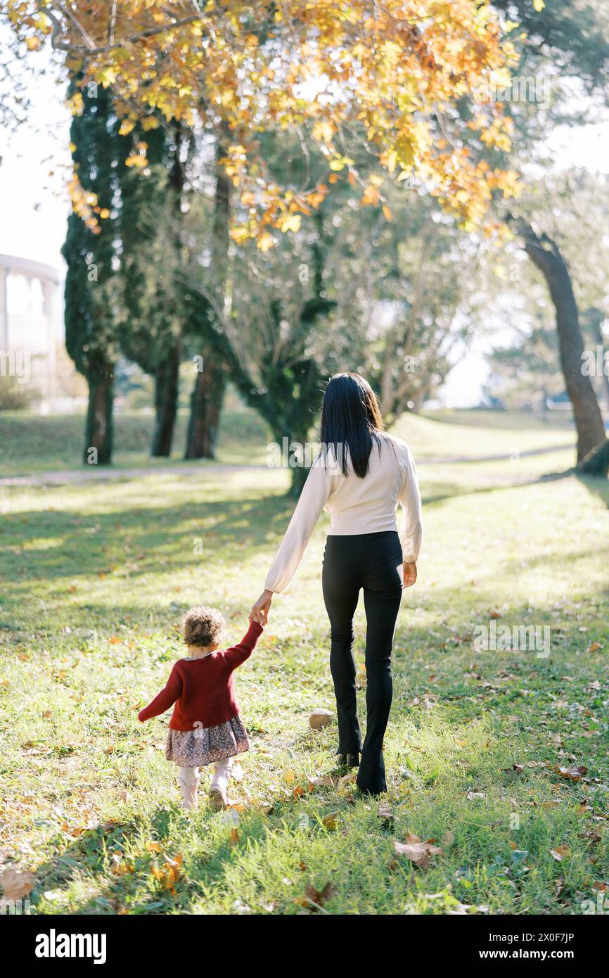 Little girl walks with her mom holding hands in the park Stock Photo ...