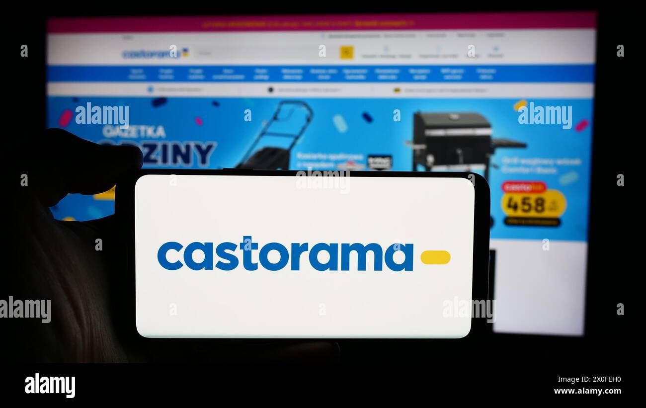 Person holding cellphone with logo of home improvement store chain company Castorama in front of business webpage. Focus on phone display. Stock Photo