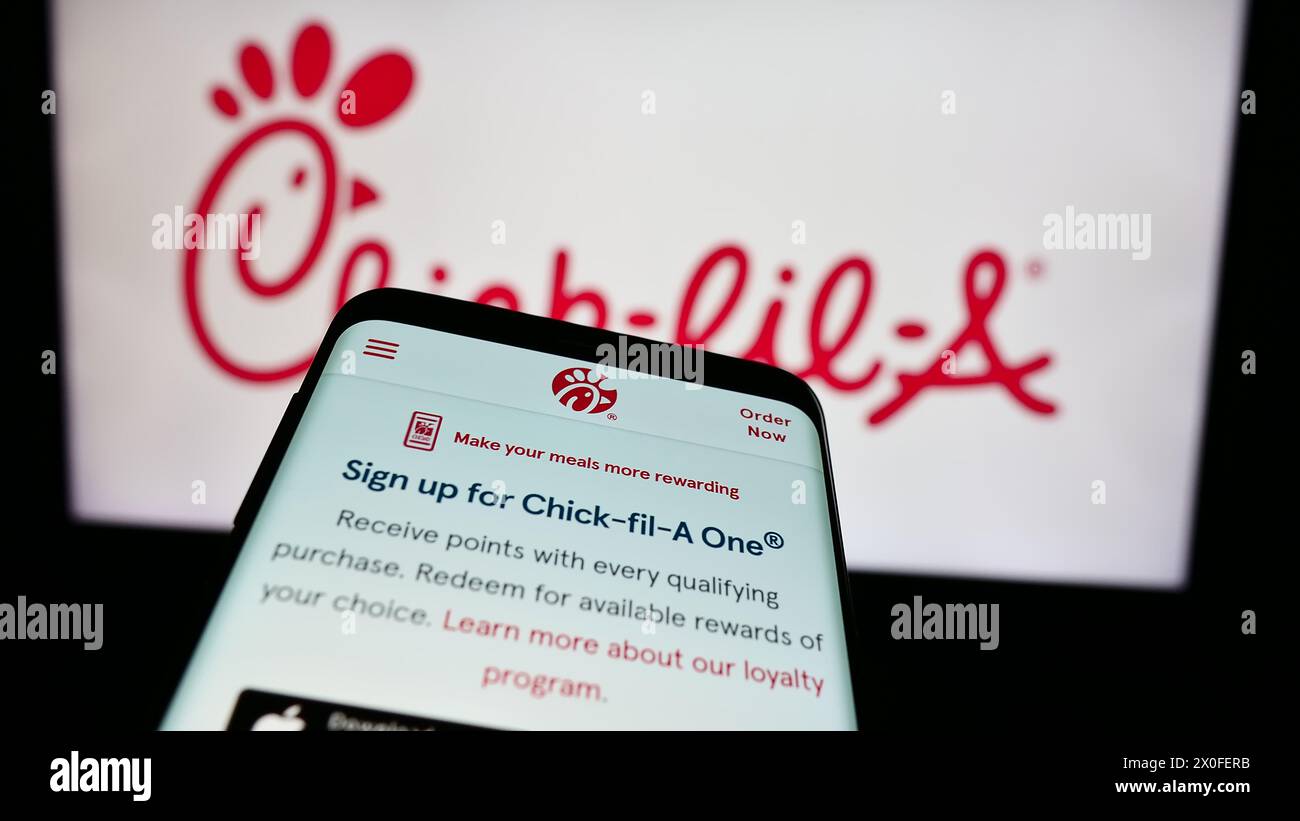 Mobile phone with website of US fast food restaurant company Chick-fil-A Inc. in front of business logo. Focus on top-left of phone display. Stock Photo