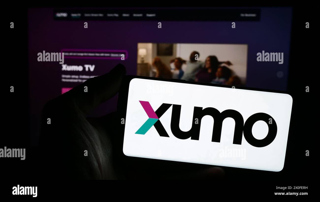 Person holding smartphone with logo of US video and television streaming company Xumo LLC in front of website. Focus on phone display. Stock Photo