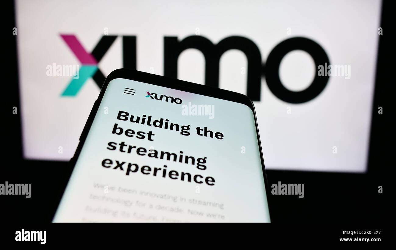 Smartphone with website of US video and television streaming company Xumo LLC in front of business logo. Focus on top-left of phone display. Stock Photo