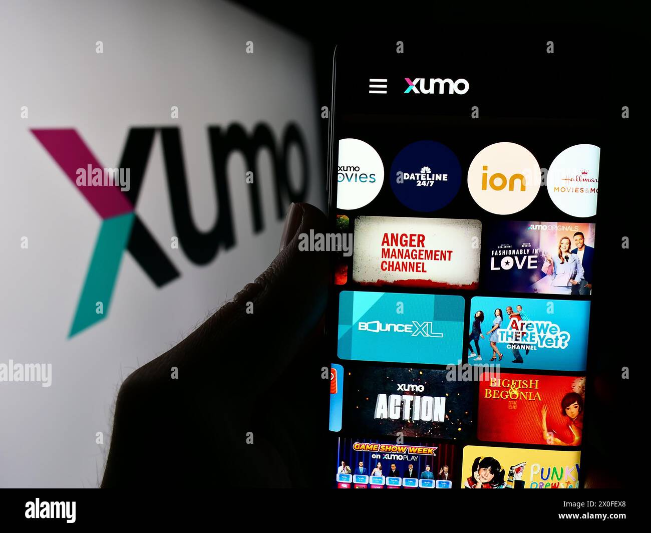 Person holding cellphone with webpage of US video and television streaming company Xumo LLC in front of logo. Focus on center of phone display. Stock Photo