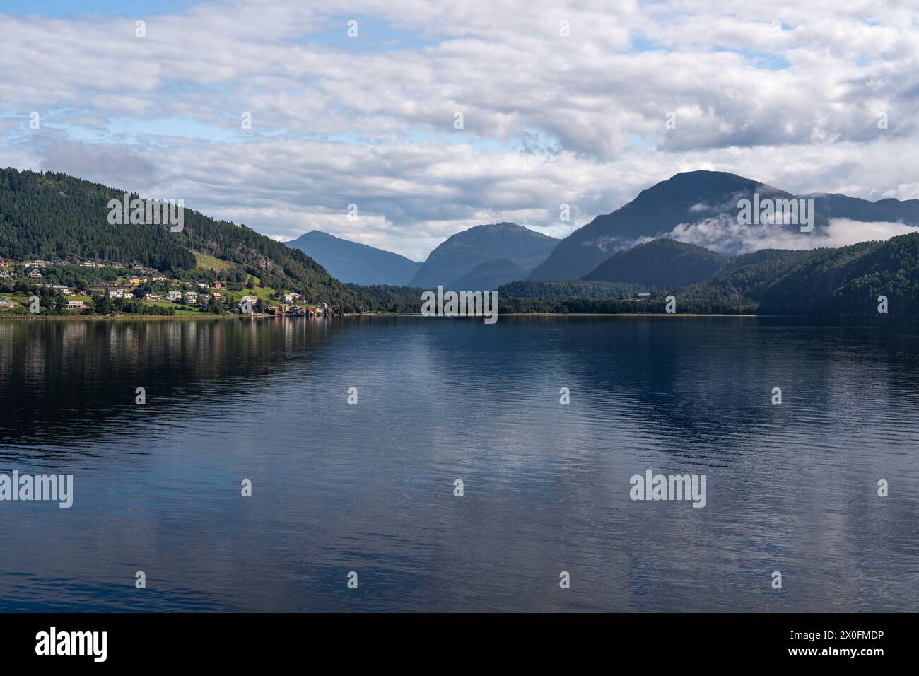 Calm waters of Stangvikfjorden mirror the sky, with the village of Kvanne nestled against the mountains. Scandinavian travel destination in summer Stock Photo