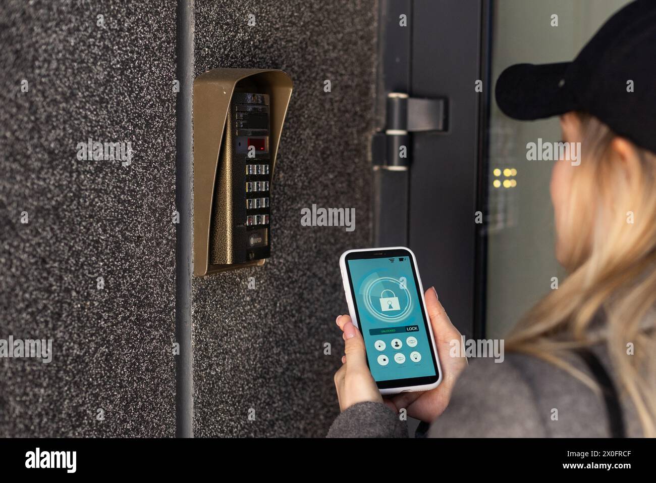 Woman locking smartlock on the entrance door using a smart phone. Concept of using smart electronic locks with keyless access. Stock Photo