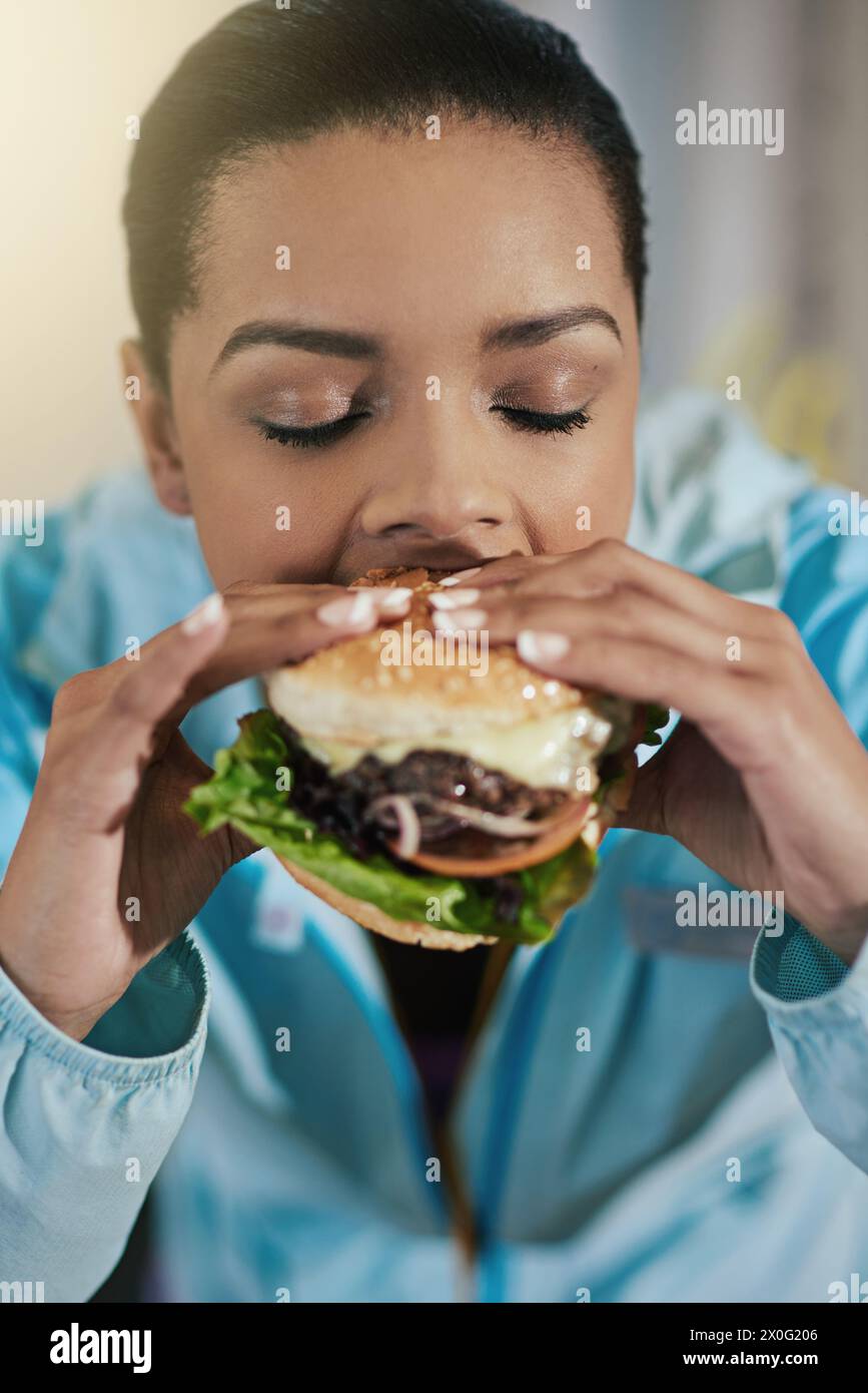 Diet, cheating and woman with burger, eating and hungry athlete with junk food for lunch after gym. Health, fitness and girl with cheeseburger for Stock Photo