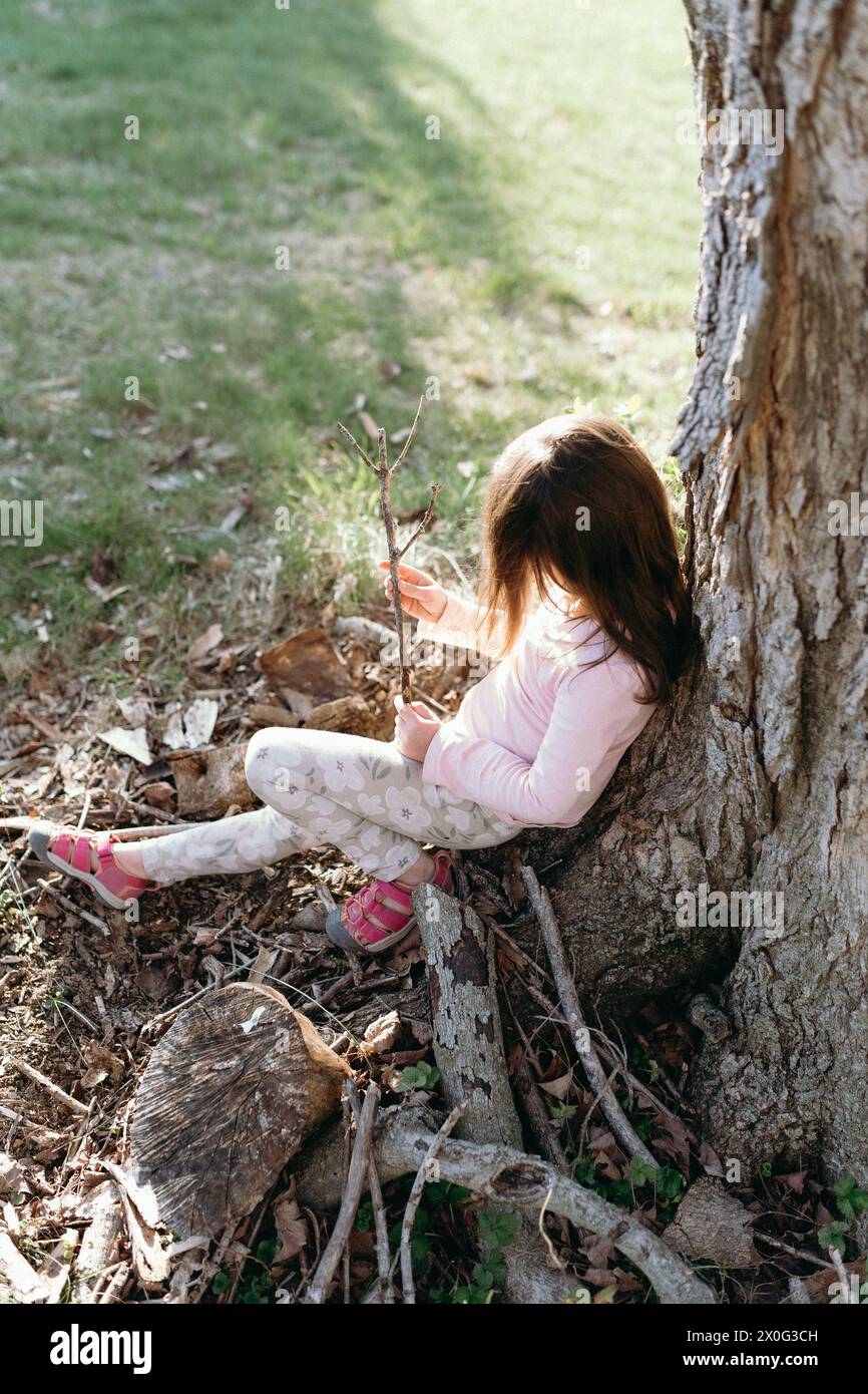 little girl sitting under a tree enjoying nature Stock Photo