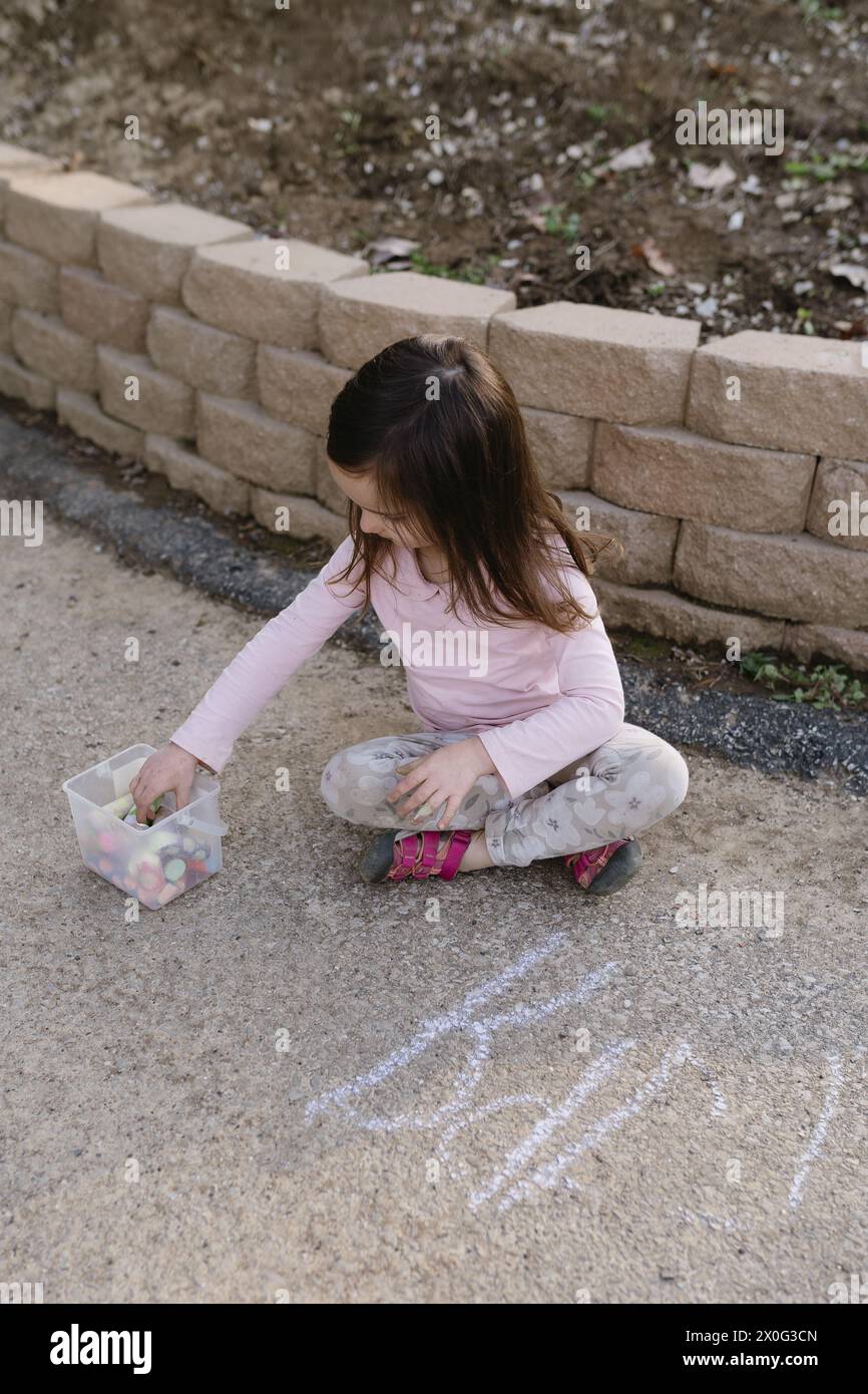 little girl sitting and drawing with sidewalk chalk Stock Photo - Alamy