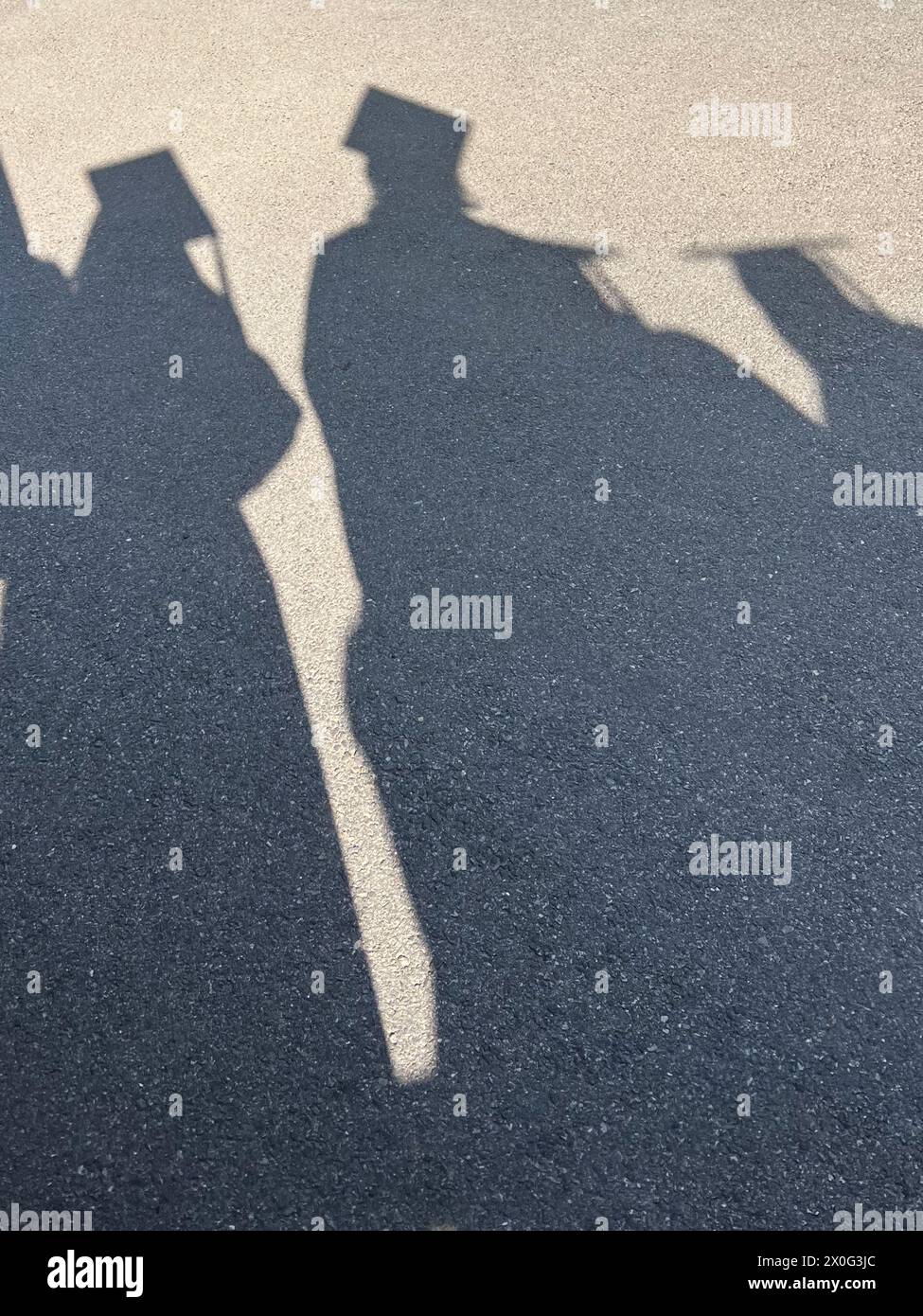 Shadows of graduates in cap and gown on pavement Stock Photo