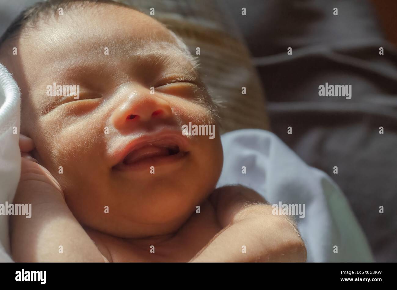 close-up of a month-old baby boy smiling with eyes shut Stock Photo