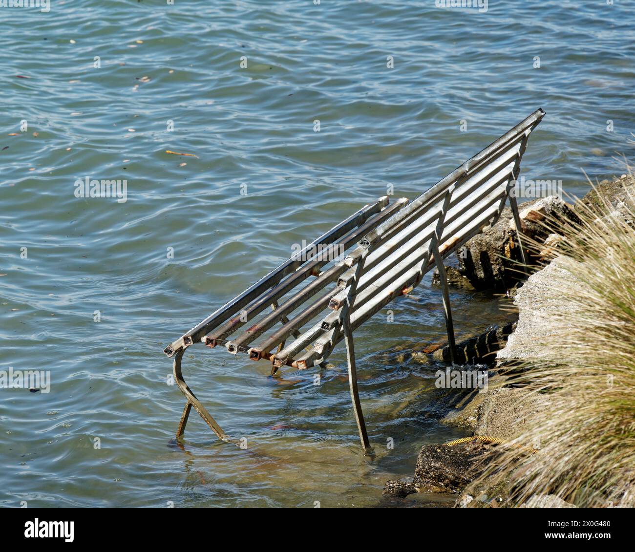 Park bench swamped by a rising sea level, Motueka, south island, Aotearoa / New Zealand's east coast. Stock Photo