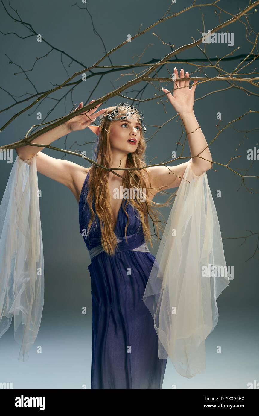 A young woman in a blue dress stands gracefully, holding a tree branch ...
