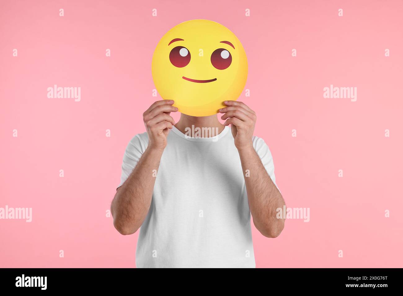 Man covering face with smiling emoticon on pink background Stock Photo