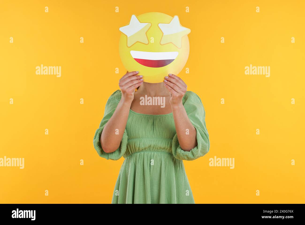 Woman holding emoticon with stars instead of eyes on yellow background Stock Photo