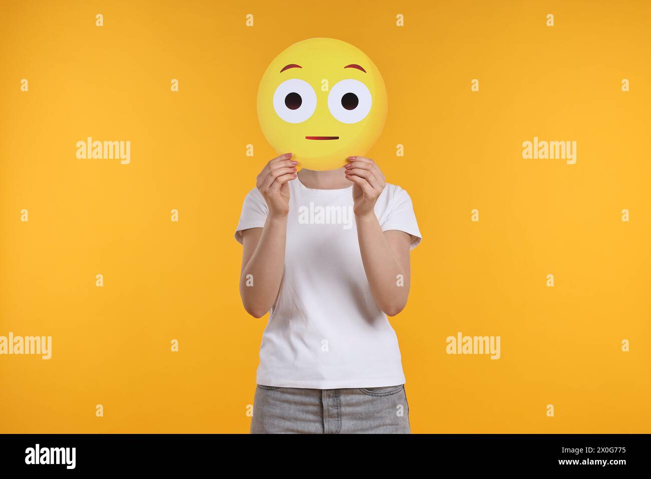 Woman covering face with surprised emoticon on yellow background Stock Photo