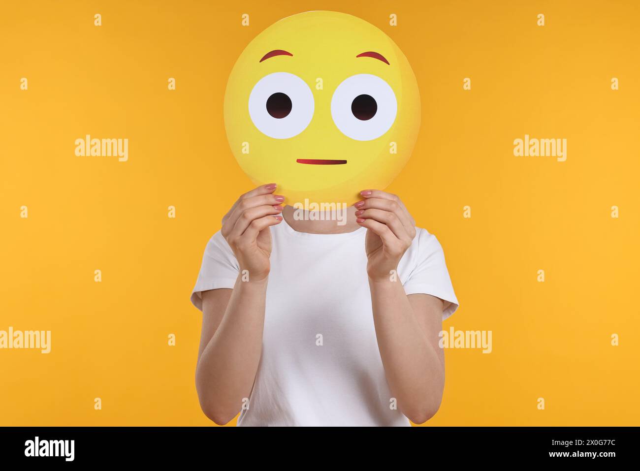 Woman covering face with surprised emoticon on yellow background Stock Photo