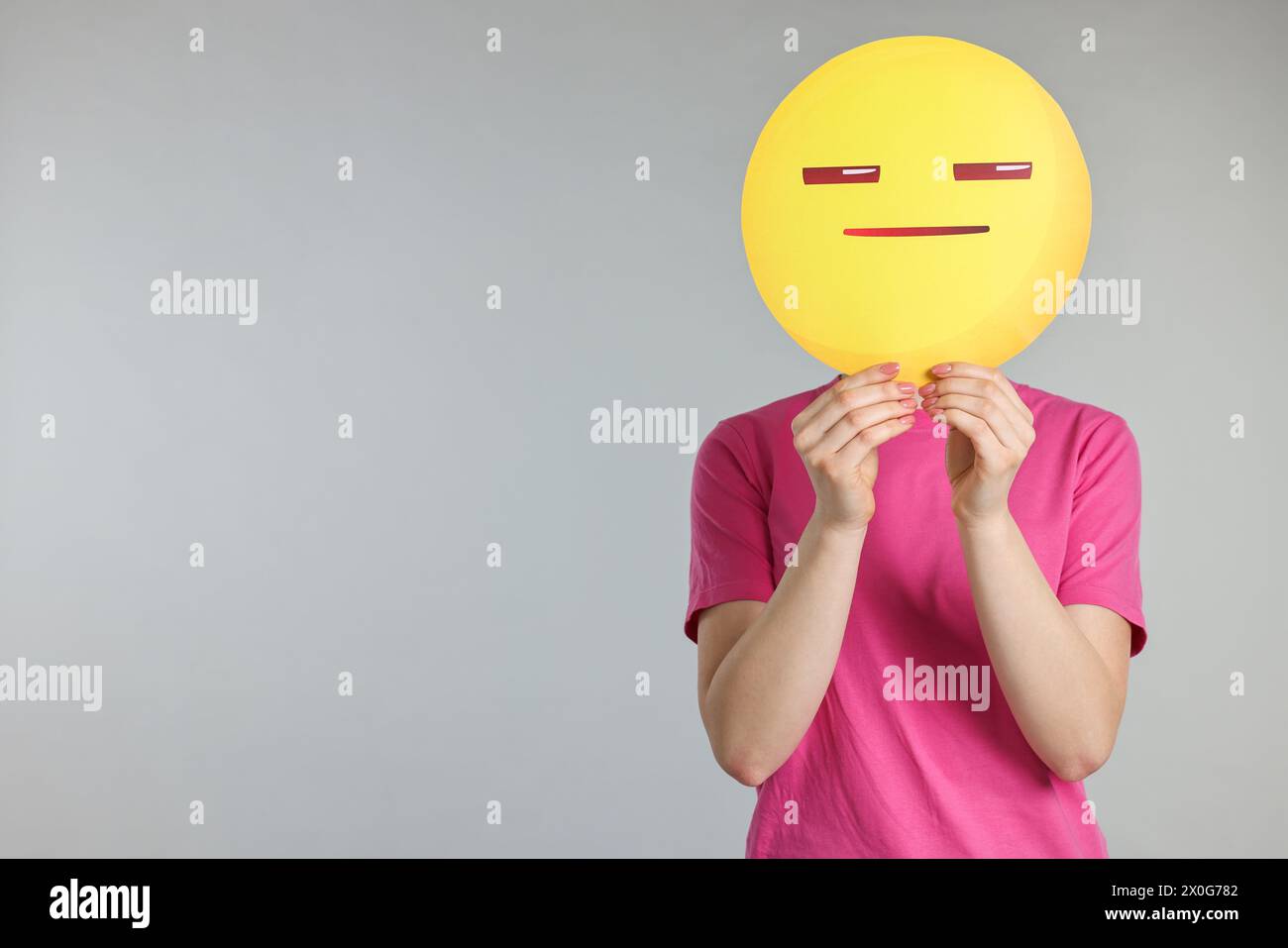 Woman holding emoticon with closed eyes and mouth on grey background. Space for text Stock Photo