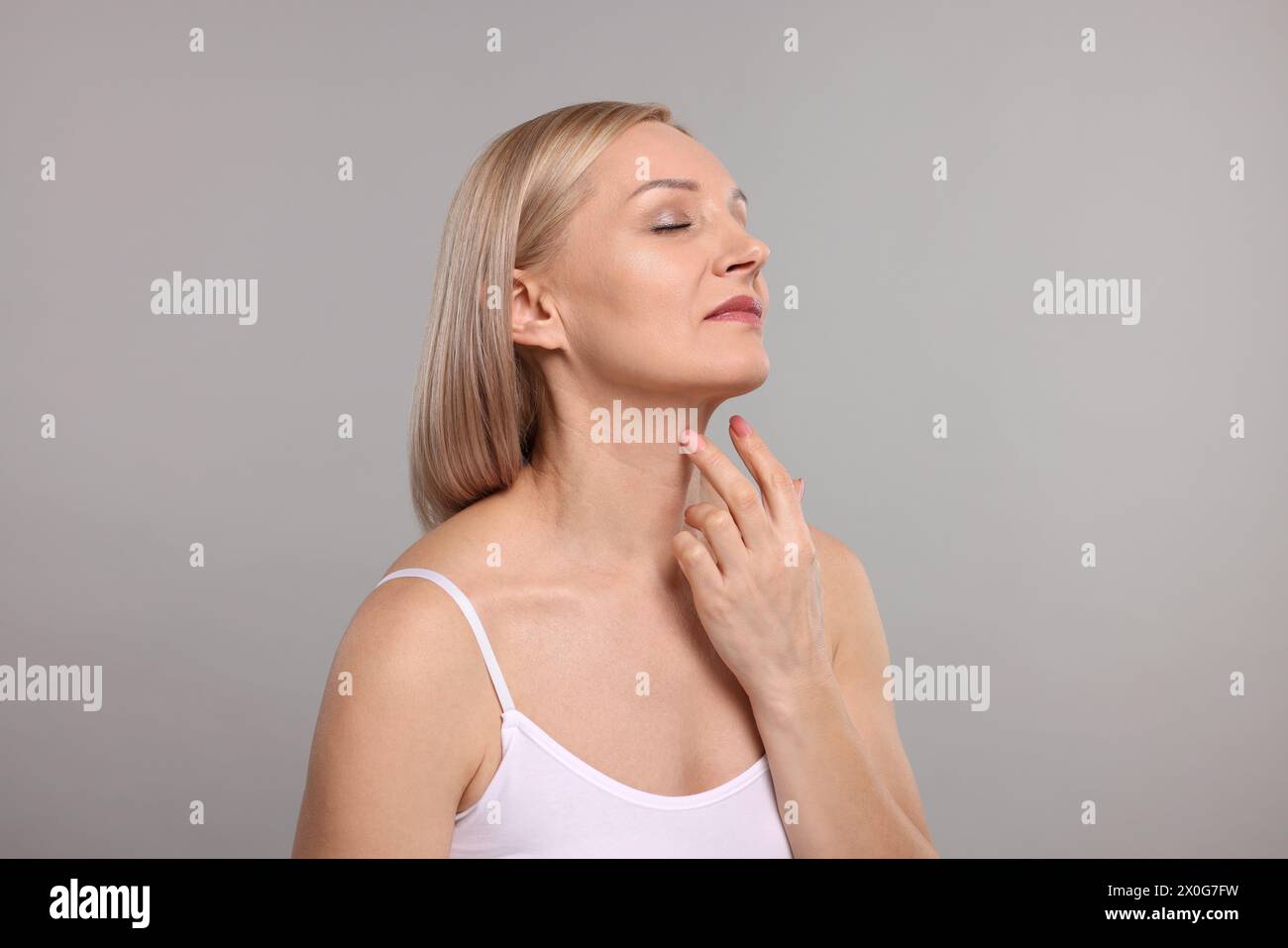 Beautiful woman touching her neck on grey background Stock Photo - Alamy