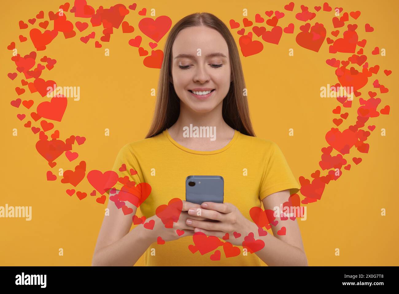 Long distance love. Woman chatting with sweetheart via smartphone on golden background. Hearts flying out of device and swirling around her Stock Photo