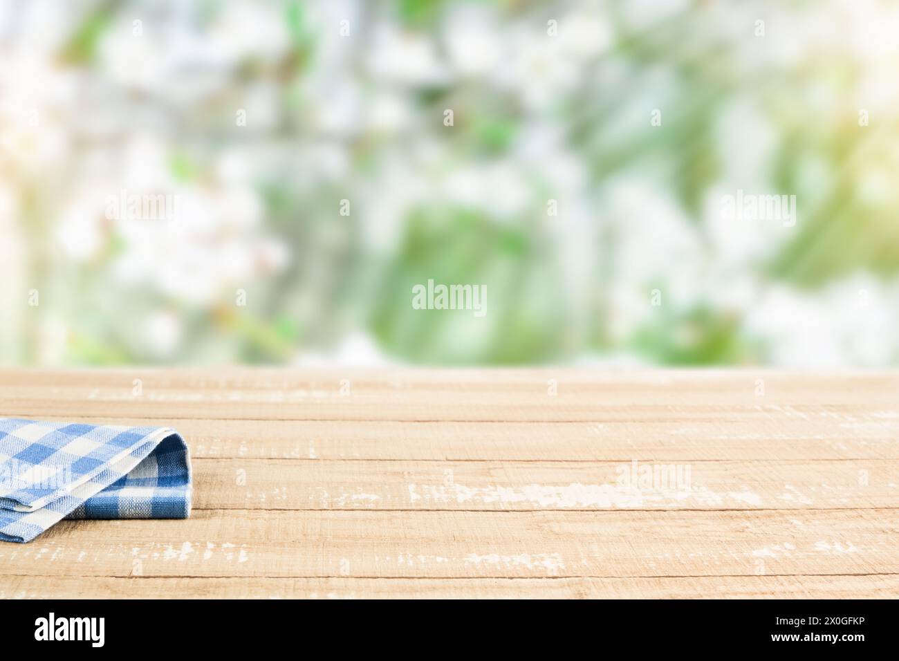 Empty rustic wooden table with blue tablecloth over blooming summer garden on sunny day background. Harvest mock up for design. Stock Photo