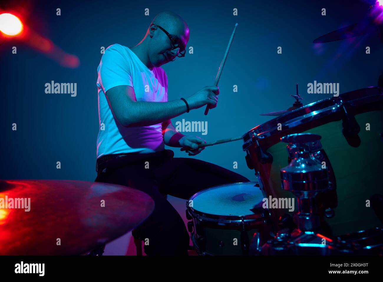 Focused bald drummer in white shirt playing in pink-purple stage ...