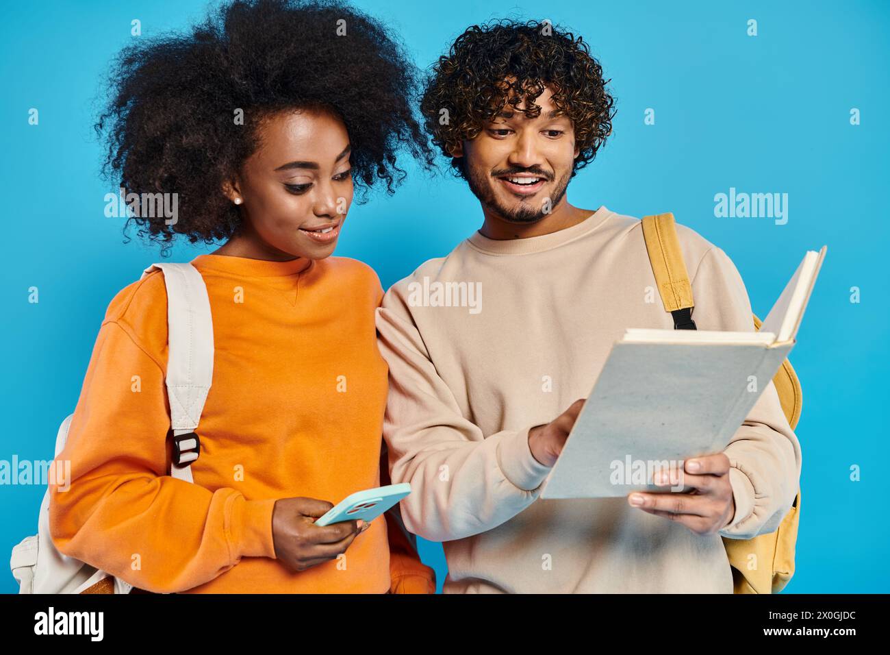 An interracial man and woman standing, examining a piece of paper together in a studio setting on a blue backdrop. Stock Photo