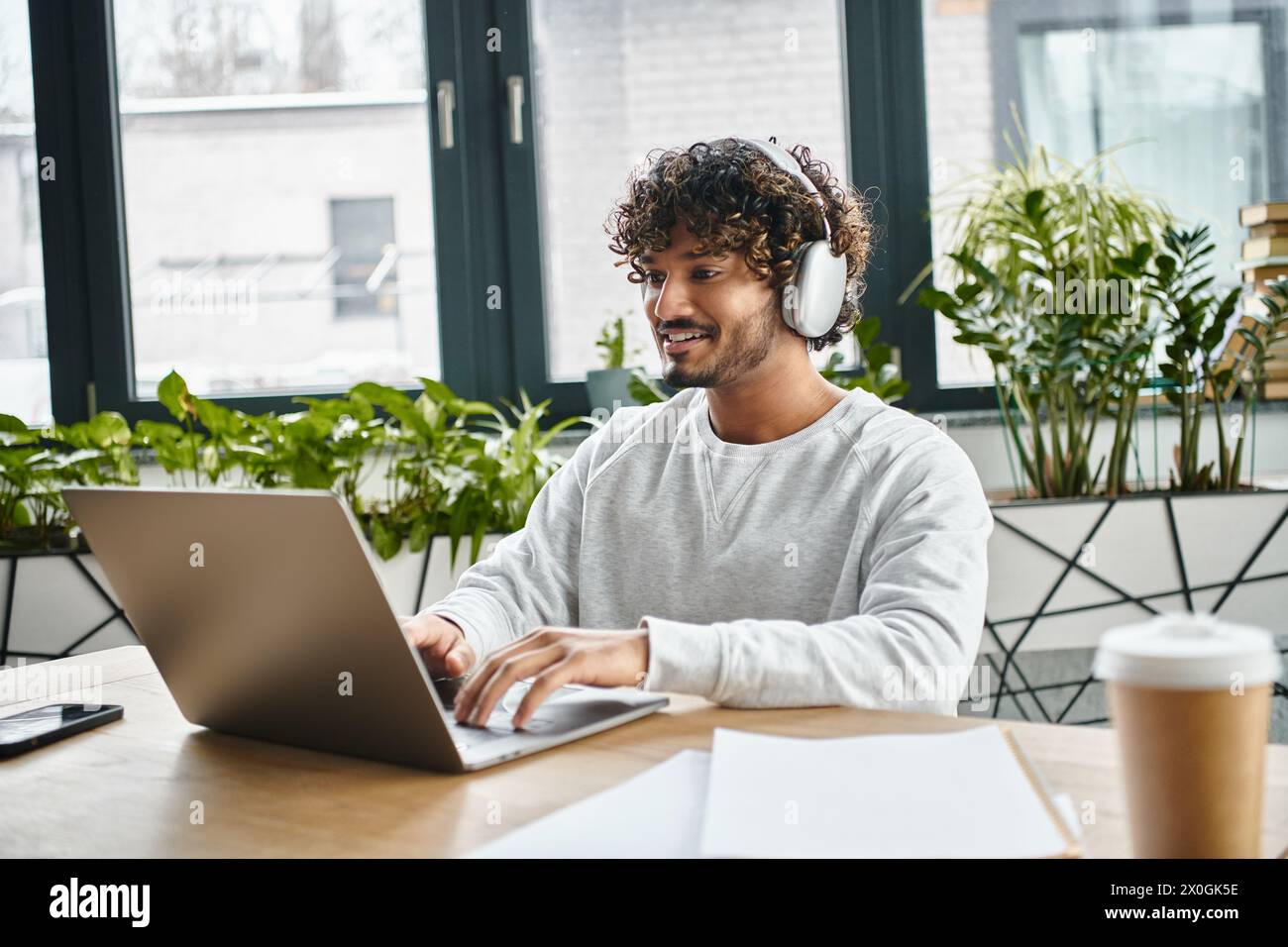 A man of diverse background sits focused in front of a laptop in a modern coworking space. Stock Photo