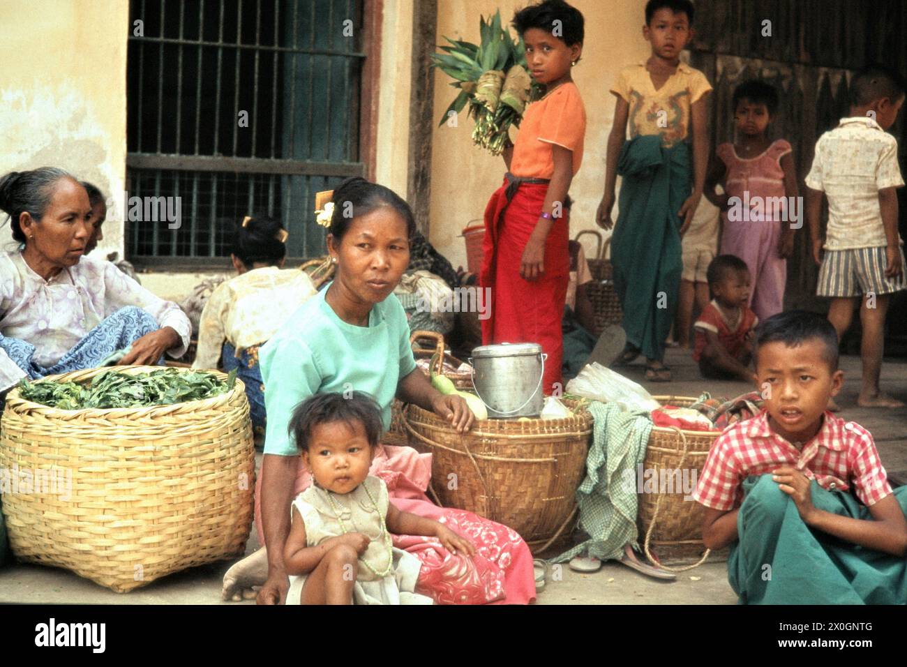 Eine burmesische Familie mit zum Verkauf bereitstehenden Produkten wartet auf den Bus an einer Straße in Bagan. Stock Photo