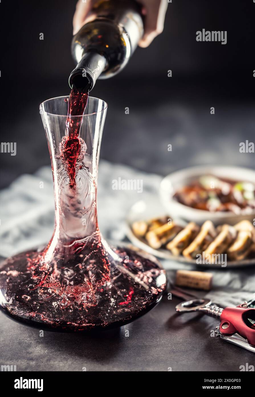 Red wine is poured from a bottle into a carafe on a table on which there is venison, Hungarian or Viennese goulash with Karlovy Vary dumplings. Stock Photo