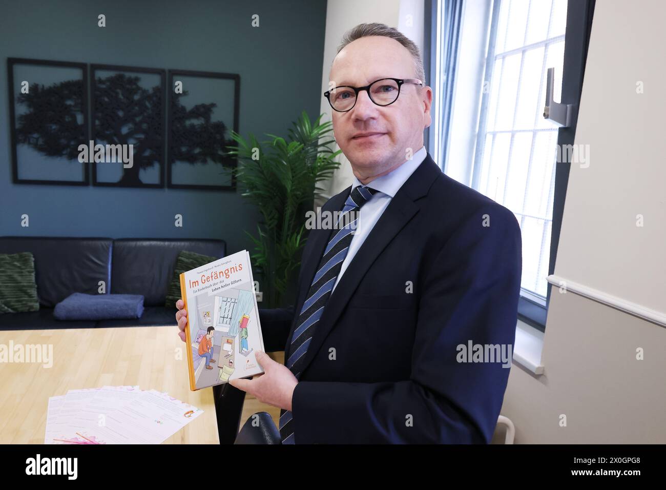 Willich, Germany. 12th Apr, 2024. North Rhine-Westphalia's Minister of Justice Benjamin Limbach holds a book entitled 'In Prison' in one of the long-term visitation rooms at Willich Prison. The Willich I and II prisons are two of six priority prisons for family-sensitive prison design in NRW. According to the Ministry, around 100,000 children in Germany are affected by the imprisonment of a parent. Credit: David Young/dpa/Alamy Live News Stock Photo