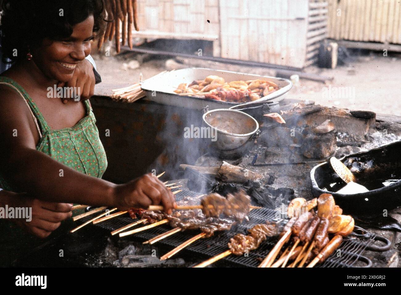 A woman puts meat and vegetable sticks on a barbecue in Machala. Stock Photo