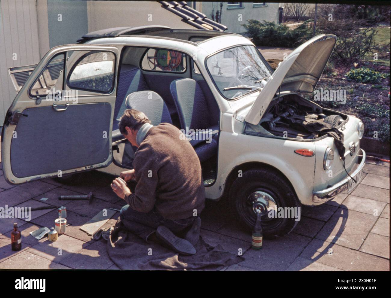 A young man repairs his Fiat 500 in the garden of his parents' house. [automated translation] Stock Photo