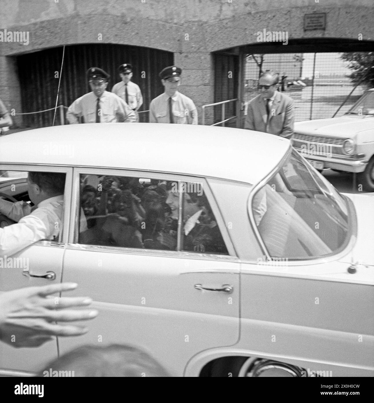 The Beatles (Paul McCartney) in a white Mercedes departing from the Munich-Riem Airport. In the back policemen. Stock Photo
