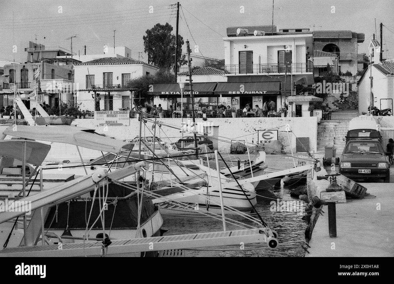 Harbor in Perdika on the island of Aegina in Greece. In the foreground there are boats and in the background customers in a restaurant. Stock Photo