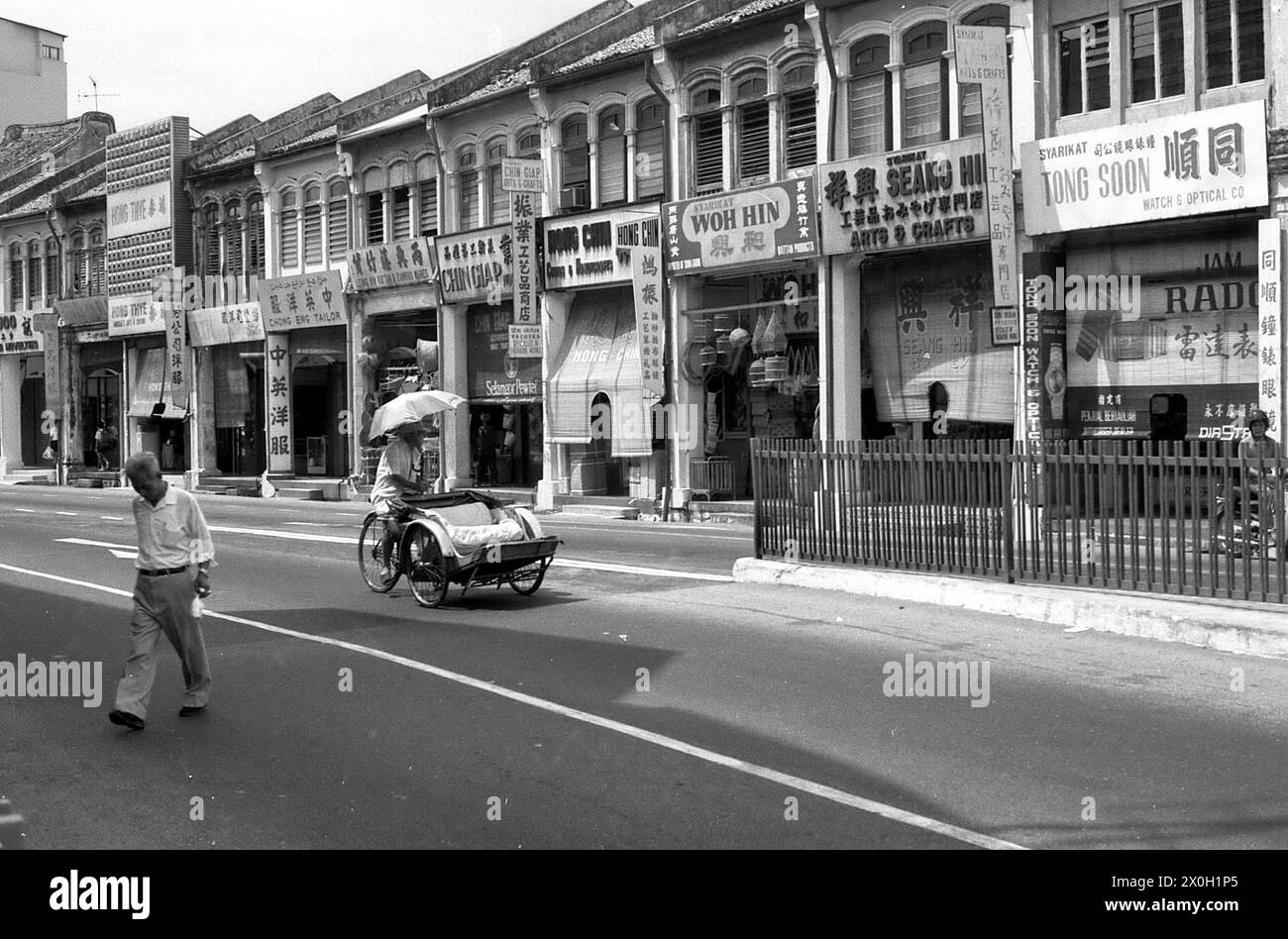 A pedestrian and a rickshaw driver with parasol in Penang in Malaysia. Stock Photo