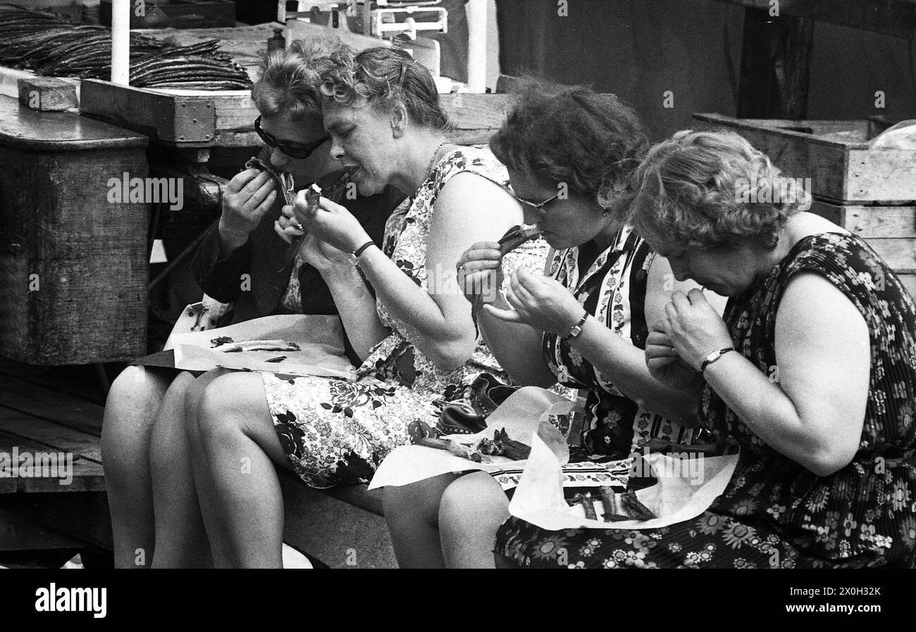 Women sit on a bench at a market in Amsterdam and eat fish. [automated