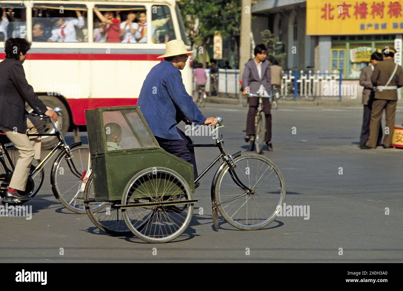 A man on a bicycle rickshaw with a child in a sidecar in Beijing. In the background an omnibus with pupils and on the right side a policeman. [automated translation] Stock Photo