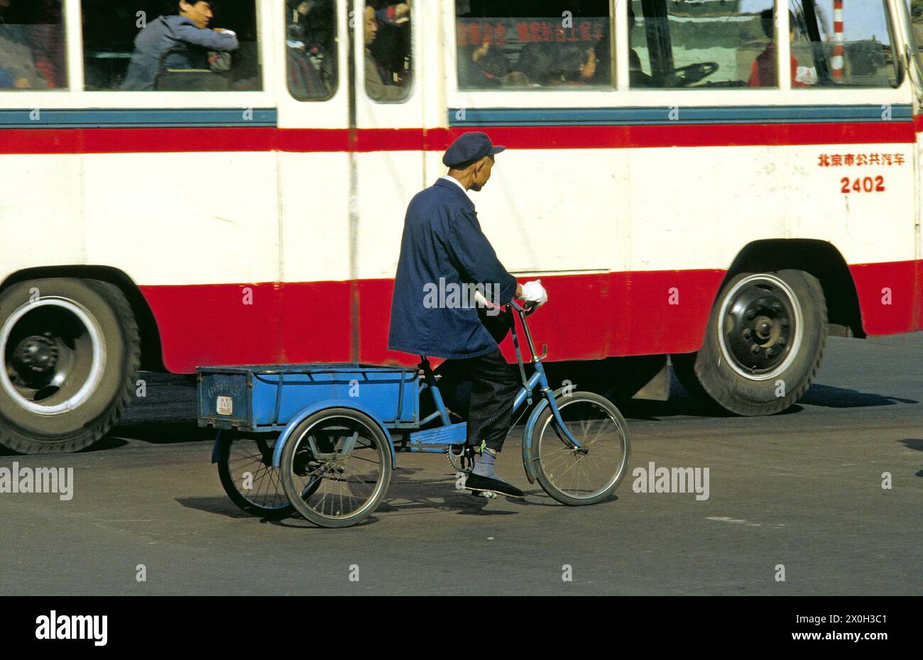 An old Chinese man on a cargo bike in downtown Beijing. In the background an omnibus. [automated translation] Stock Photo