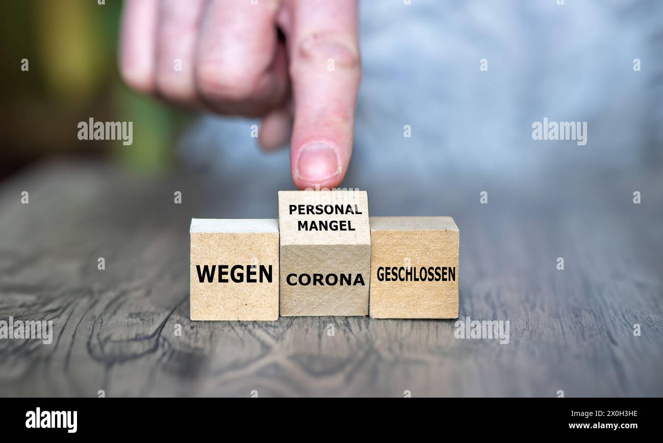 Hand turns cube and changes the German expression 'wegen Corona geschlossen' (closed due to corona) to 'wegen Personalmangel geschlossen' (closed due Stock Photo