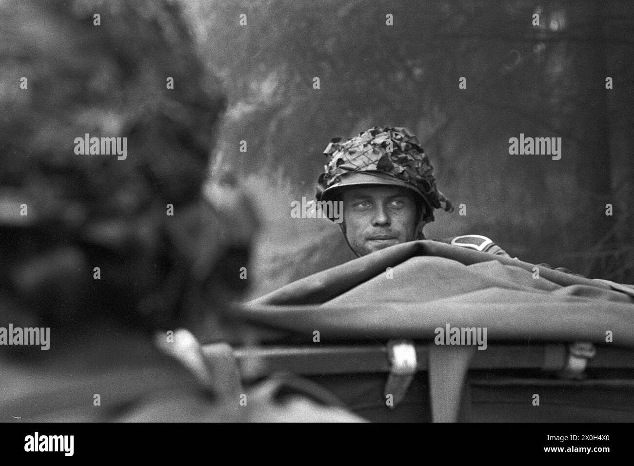 During a combat exercise, a soldier of the German Armed Forces rides on a vehicle at the head of a company and looks around to the rear. [automated translation] Stock Photo