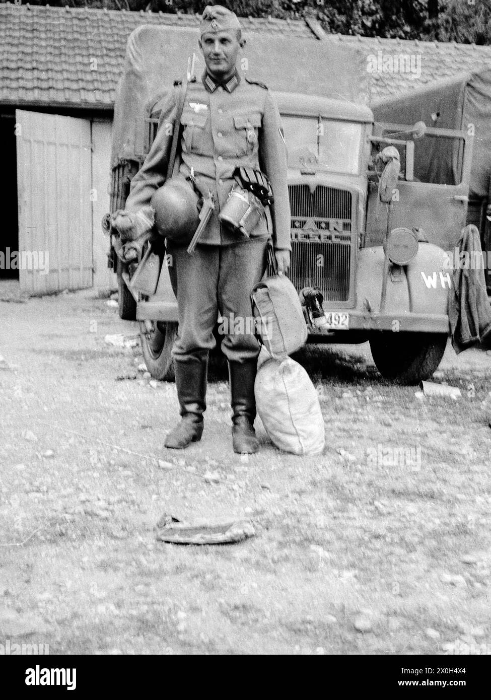 A German soldier with all his equipment poses in front of his truck, ready to leave. He is still carrying rolled-up socks in his right hand, otherwise his luggage is in two bags next to him. A flare pistol on his belt. The photo was taken by a member of the 3rd / Infantry Regiment 154 / 58th Infantry Division. [automated translation] Stock Photo