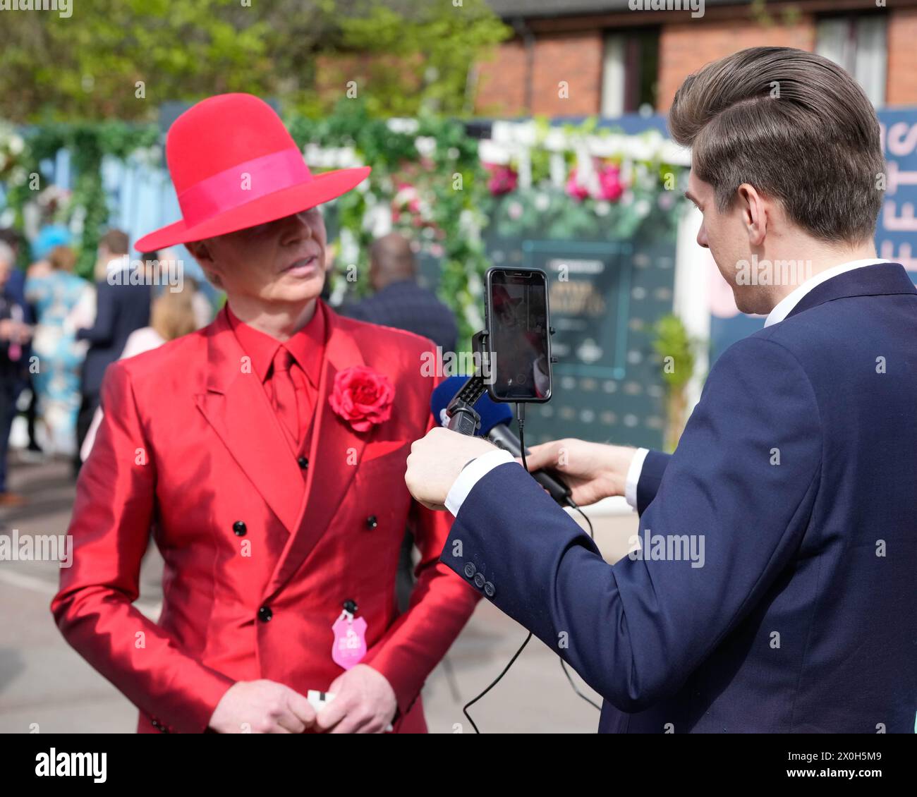 Aintree Racecourse, Aintree, Merseyside, England. 12th April 2024.  2024 Grand National Festival Day 2; A flamboyantly dressed race goer is interviewed during Ladies Day, day 2 of the festival.Photo credit: Stephen Hearn/Action Plus Sports Images/ Alamy Live News Stock Photo