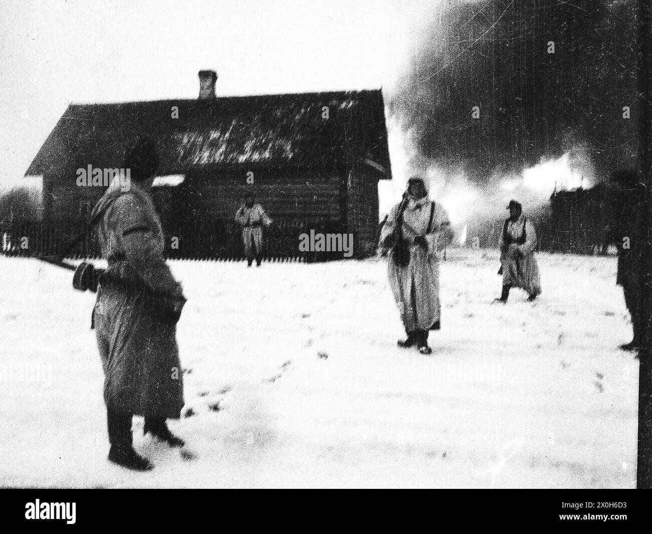Soldiers in winter camouflage leave a burning village after fighting on the Eastern Front. The picture was taken in the rear of the Eastern Front, presumably in connection with battles with partisans. The picture was taken by a member of the Raffahrgrenadier Regiment 2 / Rahdfahrsicherungsregiment 2, in the northern section of the Eastern Front. [automated translation] Stock Photo