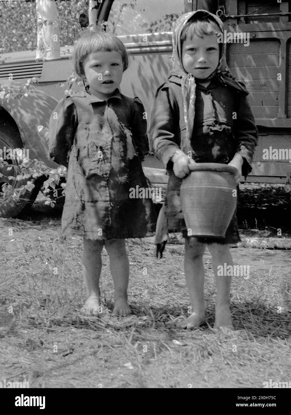 Two little girls in simple and patched clothes are standing in front of a Wehrmacht vehicle. The girl with the headscarf is carrying a clay jug. The picture was taken by a member of the Radfahrgrenadierregiment 2 / Radfahrsicherungsregiment 2, on the Eastern Front. [automated translation] Stock Photo