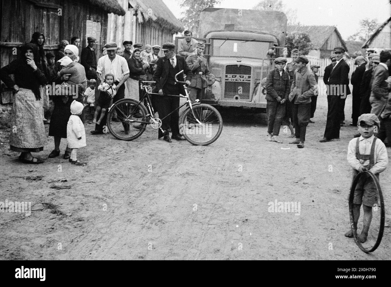Villagers have gathered on the street. There are women, men and children. A boy is playing with a bicycle rim. Wehrmacht soldiers stand around their truck smoking. The picture was taken by a member of the Radfahrgrenadierregiment 2 / Radfahrsicherungsregiment 2, on the Eastern Front. Presumably during the advance in the summer of 1941 [automated translation] Stock Photo